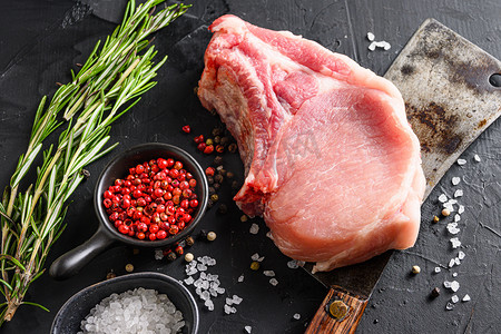 肋骨上的有机炸肉排或猪肉上的美国经典屠夫刀或切肉刀，黑色石板桌面上有香料、迷迭香和红辣椒。