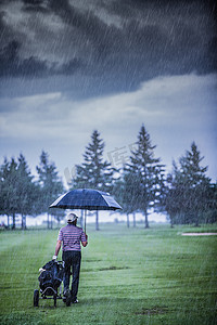 秋天雨天摄影照片_高尔夫球手在雨天离开高尔夫球场