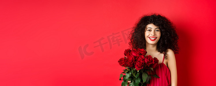快乐时尚的女模特，带着一束红玫瑰，面带微笑，对着镜头、工作室背景开朗