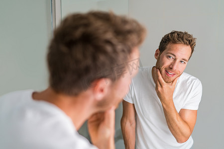 男性美女年轻人摸着胡子，看着镜子里的脸-健康的皮肤。