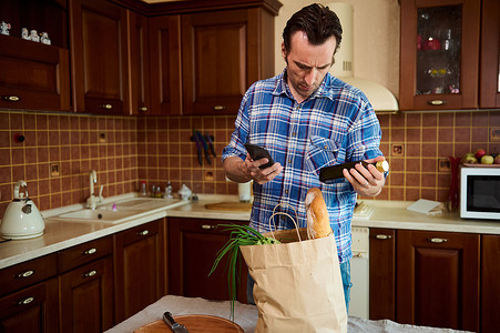 运动型男用油阅读瓶子上的成分，同时在家里的厨房里打开杂货购物袋