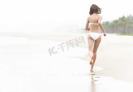 漂亮的女人沿着海滩在湿沙上奔跑。