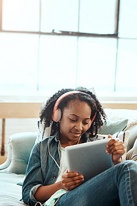 平板电脑、耳机和沙发上的黑人女孩一边听音乐、收音机或播客一边放松。