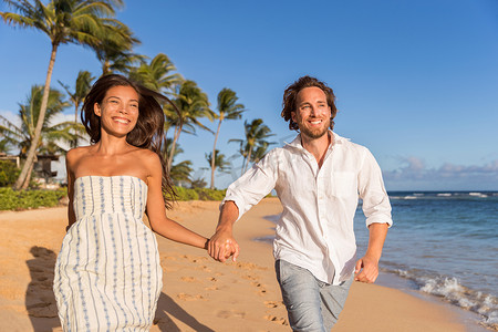 幸福的新婚夫妇手牵着手在沙滩上奔跑，度蜜月旅行。