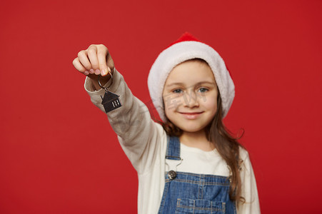 寒假安全摄影照片_专注于一个戴着圣诞帽的可爱女婴手中的钥匙链，她拿着新房、住所的钥匙。