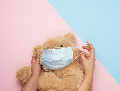 蓝色粉红色背景中戴着医用口罩的大泰迪熊，让步