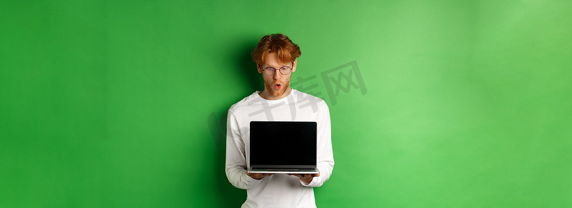 戴着眼镜的红发书呆子给人留下了深刻的印象，他展示了空白的笔记本电脑屏幕，惊讶地看着显示屏，站在绿色背景上