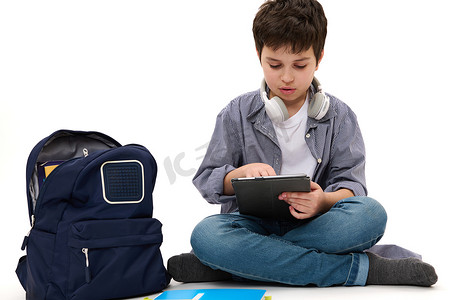 英俊的少年男学生穿着休闲服，使用数字平板电脑，在白色背景下在线学习。