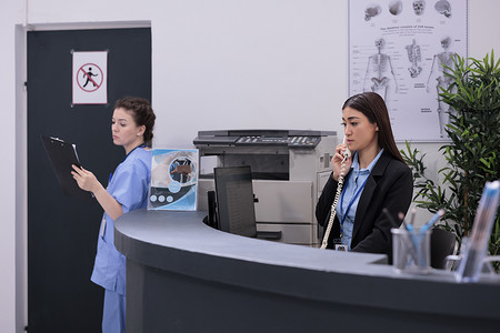 站在接待台的亚洲接待员通过固定电话与远程病人交谈