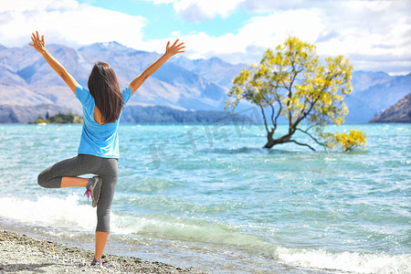 新西兰晨间瑜伽女孩在瓦纳卡湖做树式变体练习瑜伽，在瓦纳卡湖边，这棵孤树是新西兰旅游的热门景点。