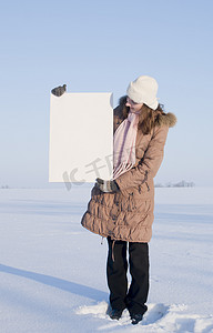 冬天海报摄影照片_在冬天雪地里拿着白色海报的女孩