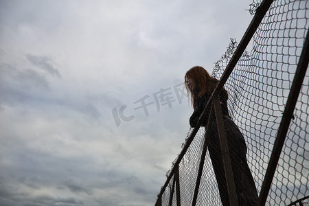 一个十几岁的女孩独自站在码头上在码头孤独试图孤立以应对愤怒并在傍晚找到力量撞上铁栅栏阴沉的照片放弃思考命运是不容易和艰难的