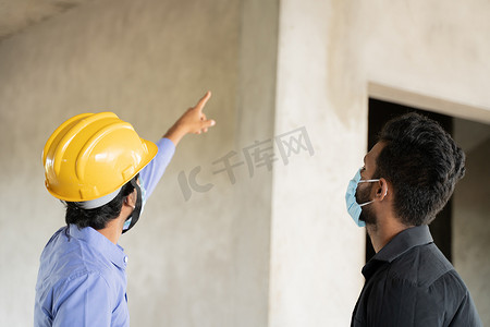 两名戴着医用口罩的建筑工人忙于工作，同时保持社交距离 — Covid-19 或工作场所冠状病毒安全措施的概念。