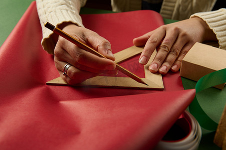 女人的手用木蜡笔和三角尺在包装纸上画画，计算包装礼物的数量