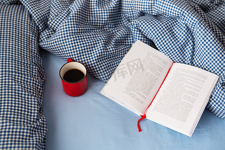红2021摄影照片_乌克兰，罗夫诺 — 2021 年 8 月 11 日：在寒冷的冬日，床上铺着一条舒适的毯子、一本打开的书和一杯热红咖啡的顶视图。