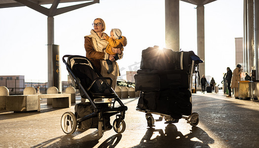 Motherat 带着他的婴儿男婴旅行，在机场航站楼前散步、推着婴儿车和行李车。