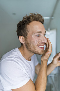 男人在脸上涂上眼霜，照顾他的皮肤，在家里进行抗衰老治疗。
