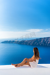 豪华旅游度假的欧洲旅游女性在希腊圣托里尼岛的豪华酒店度假村阳台上放松身心，欣赏地中海和伊亚的美景。