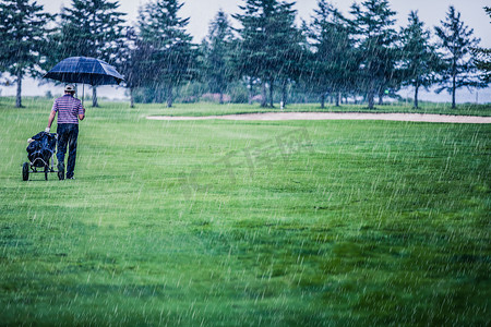 秋天雨天摄影照片_高尔夫球手在雨天离开高尔夫球场