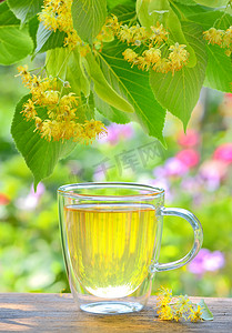 木桌上有菩提树茶和鲜花的杯子
