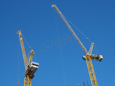 在蓝天的建筑工地上工作的两台高大的黄色塔式起重机