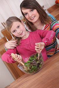 年轻女人和小女孩在碗里搅拌蔬菜沙拉