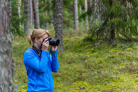 年轻女子在树林间徒步旅行并用相机拍照。