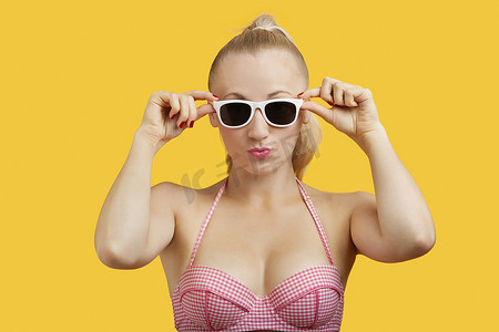 黄色背景中一位戴着太阳镜、嘴唇皱起的漂亮年轻女子的画像