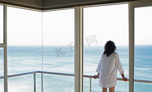 从度假村的阳台看海景的年轻女子的后视图