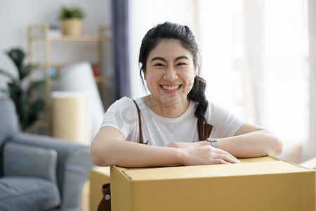 箱子摄影照片_带着箱子搬家时，快乐的女人在家里微笑