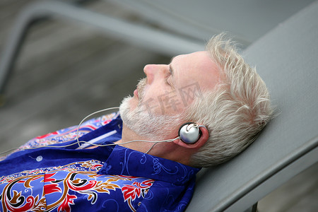 沉闷摄影照片_躺在躺椅上听音乐的男人