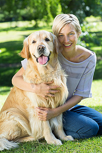 抱狗摄影照片_快乐的金发女郎在公园里抱着她的狗