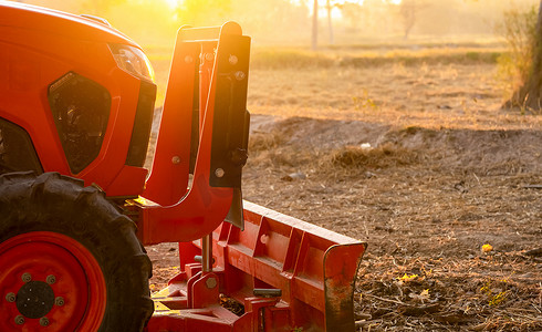 橙色拖拉机在阳光明媚的夏日早晨停在水稻农场。