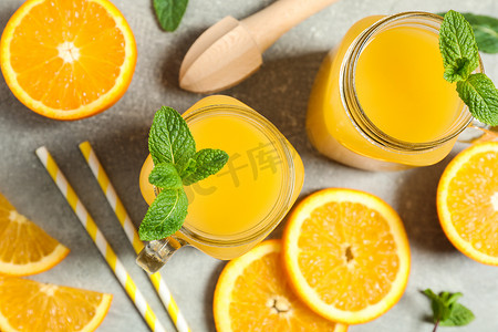 小管摄影照片_由橙片、薄荷、小管、木制榨汁机和玻璃罐组成，灰色背景为新鲜橙汁，特写。