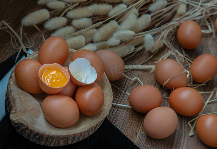 新鲜鸡蛋（鸡蛋）上的碎鸡蛋放在小木材上，干花放在黑桌上。