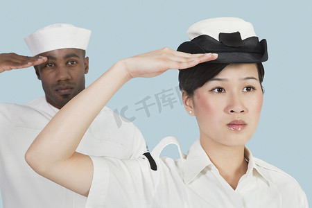 海军敬礼摄影照片_严肃的美国海军女军官和男水手在浅蓝色背景下敬礼的画像