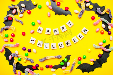 蝙蝠横幅摄影照片_木块上的铭文 Happy Halloween 和用纸制自制蝙蝠和五颜六色的糖果和软糖蠕虫制成的框架