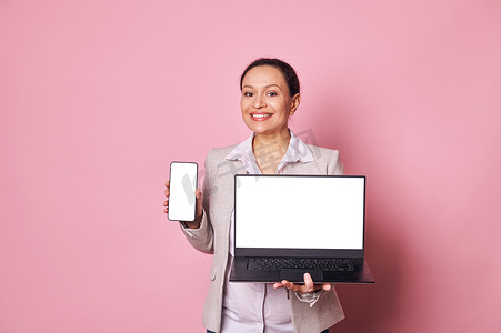 愉快的怀孕女商人展示智能手机和带白色数字屏幕的笔记本电脑，带有广告或移动应用程序模型