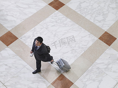 一位商人带着手提箱在瓷砖地板上行走的高视图