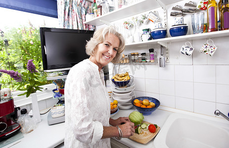 在厨房柜台切新鲜蔬菜的快乐老年妇女的画像