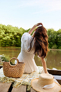 洋湖摄影照片_特写照片：一位女士背对着镜头坐在湖岸边，手里拿着一个装满雏菊的柳条袋