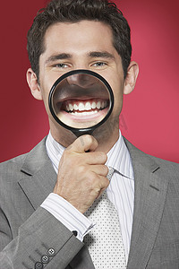 红色背景下一位商人拿着放大镜对着微笑的嘴巴的特写