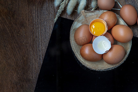 新鲜鸡蛋（鸡蛋）上的碎鸡蛋放在小木材上，干花放在黑桌上。