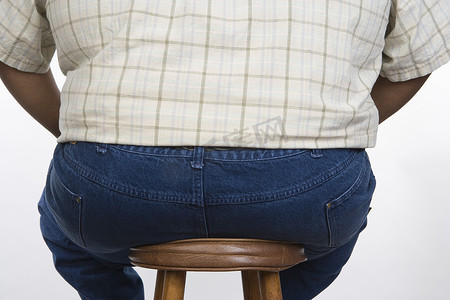 坐在凳子上的肥胖男子的后视图在白色背景下被隔离