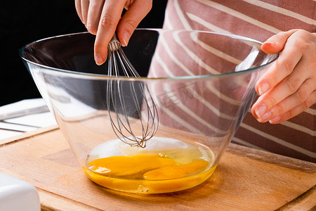 关闭一个女人的手搅打鸡蛋在厨房的木桌上做面团。