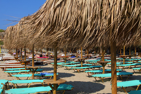 蓝色大海附近的海滩，配有日光浴床和遮阳伞