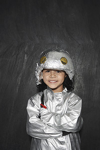 儿童宇航服摄影照片_一个穿着铝箔宇航服的可爱小男孩的肖像，双臂交叉在黑色背景下