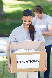捐款箱摄影照片_快乐的黑发志愿者拿着捐款箱