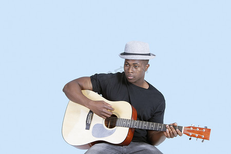 器材音乐摄影照片_浅蓝色背景中弹吉他的年轻非洲裔美国人