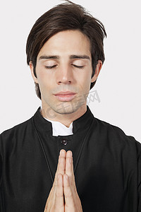 节灰色摄影照片_穿着牧师服装的年轻人在灰色背景下祈祷